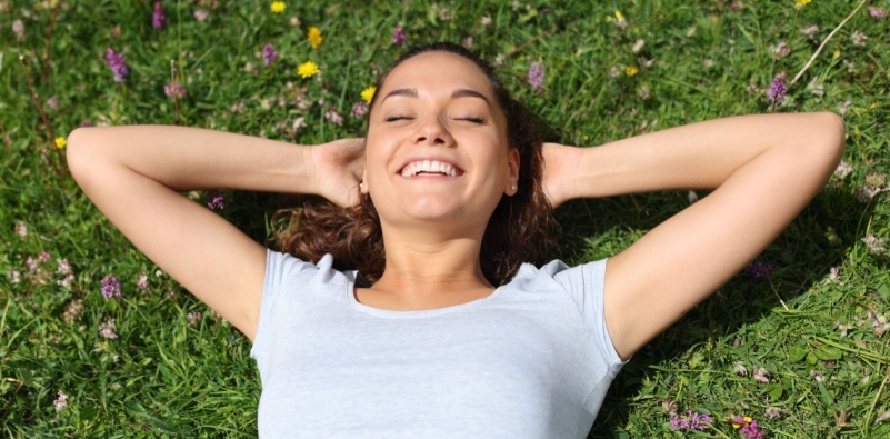 A woman smiling, with her eyes closed, while lying on the grass in a field with flowers