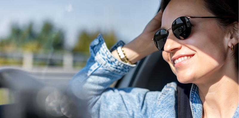 A woman wearing a pair of sunglasses whilst driving in bright, sunny conditions.