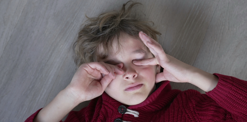 Child lying on the floor rubbing tired or irritated eyes, illustrating eye discomfort and fatigue