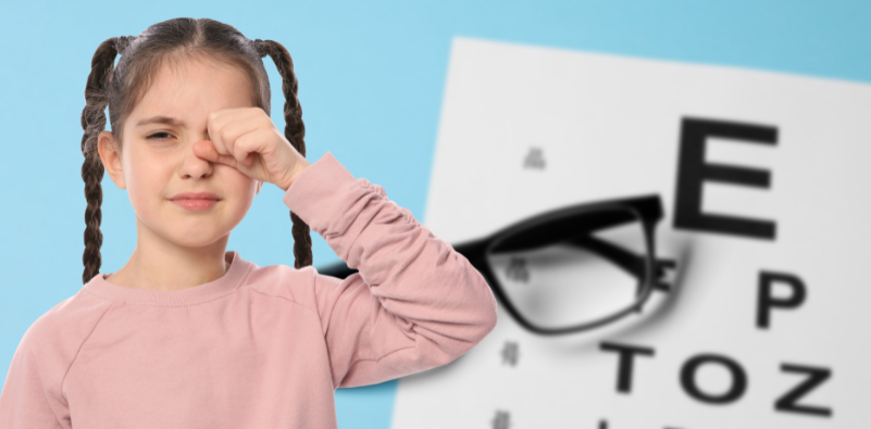 Girl rubbing her eye with a Snellen eye chart and glasses in the background, illustrating children’s eye health and vision concerns